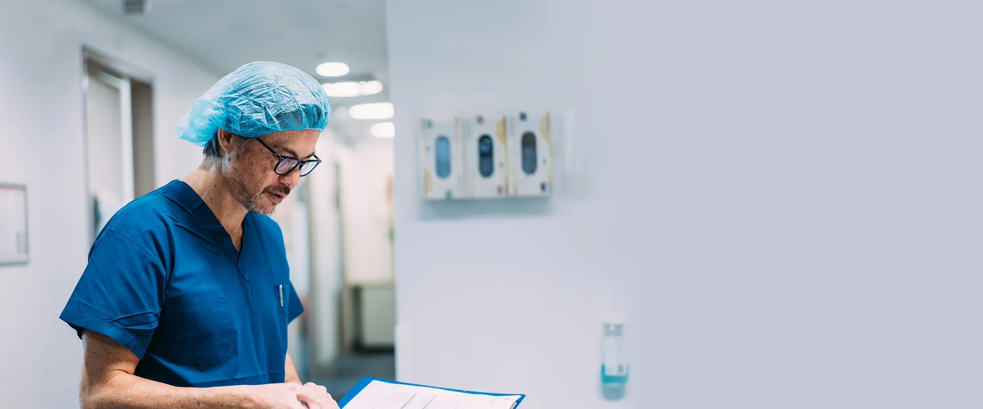 Surgeon in scrubs reviewing patient notes in a clinic hallway